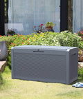 Huge 100 Gallon Outdoor Resin Deck Box With Lockable Lid For Patio Furniture Cushions Garden Tools And Pool Supplies Waterproof Weatherproof Storage With Large Capacity Dark Grey placed on a lawn by flowers.