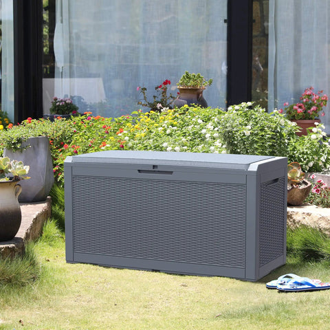 Huge 100 Gallon Outdoor Resin Deck Box With Lockable Lid For Patio Furniture Cushions Garden Tools And Pool Supplies Waterproof Weatherproof Storage With Large Capacity Dark Grey placed on a lawn by flowers.