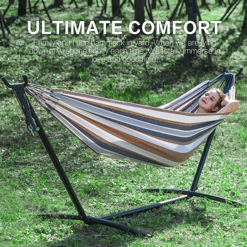 Person relaxing in a double hammock with stand for outdoor and indoor use portable space saving heavy duty steel frame easy assembly 2 person capacity 450 lbs kick back coffee