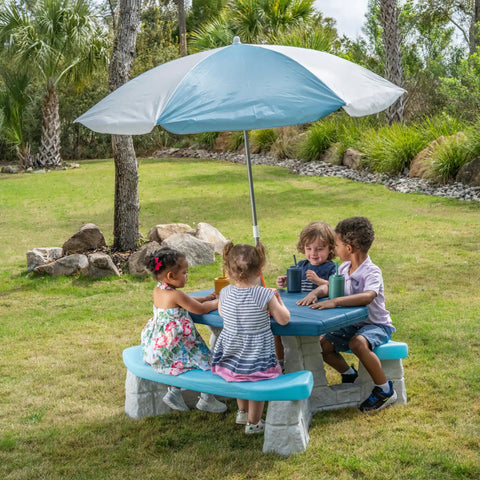 Sun And Fun Picnic Table With Umbrella For Indoor And Outdoor Use Toddler Sized Table With Five Foot Shade Canopy That Blocks UVA And UVB Rays For Safe Chill Backyard Fun with kids seated under blue and white canopy