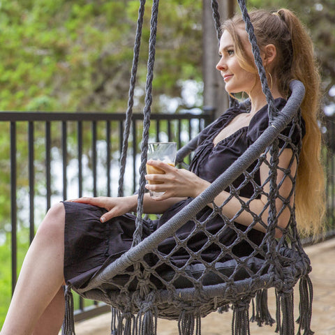 Woman sitting in Chill Out Hammock Chair With Macrame Swing, Handwoven Cotton Rope, enjoying outdoor view.