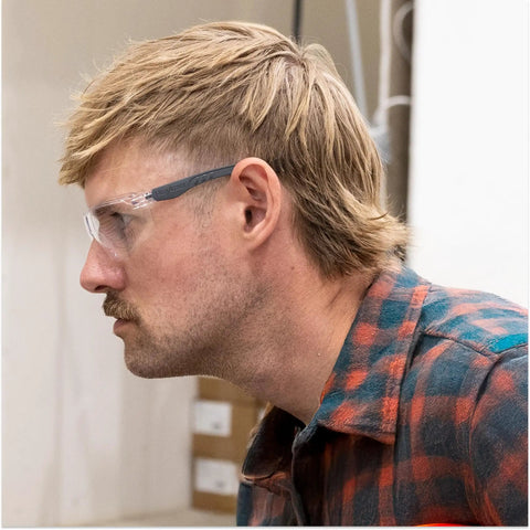 Kickass Rimless Wraparound Safety Glasses With Ultra Light Twenty One Gram Flex Plus Heavy Duty Dust Defense And Never Fog Tech For Top Shelf Eye Armor On Every Work Shift worn by a man in profile view.