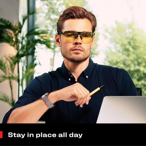 Man wearing Yellow Safety Glasses For Men, ANSI Z87 Rated Shooting Eyewear, inside office, seated with laptop.