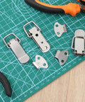 Stainless Steel Toggle Latch Set With Spring Loaded Mechanism pieces displayed on a green cutting mat with tools.