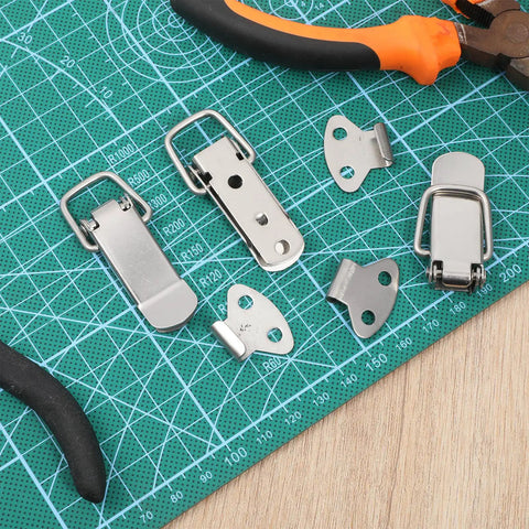 Stainless Steel Toggle Latch Set With Spring Loaded Mechanism pieces displayed on a green cutting mat with tools.
