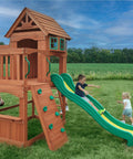 Children playing on Atlantis Cedar Wood Swing Set With Wave Slide And Raised Clubhouse Featuring Rock Wall in backyard