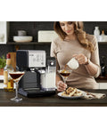 Woman using Super Sleek Programmable Espresso And Cappuccino Maker Featuring Automatic Milk Frother And 19 Bar Pump on kitchen counter.