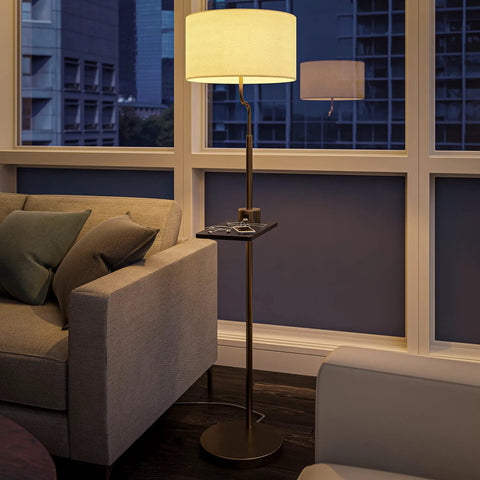 Brass Finish USB Floor Lamp With Built In Tray And USB Port beside a couch in a modern living room with window view.