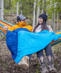 Couple in hammocks using ThermaQuilt Hammock Underquilt 40F 3 In 1 Go-To System For Outdoor Sleep, hiking boots, forest setting.