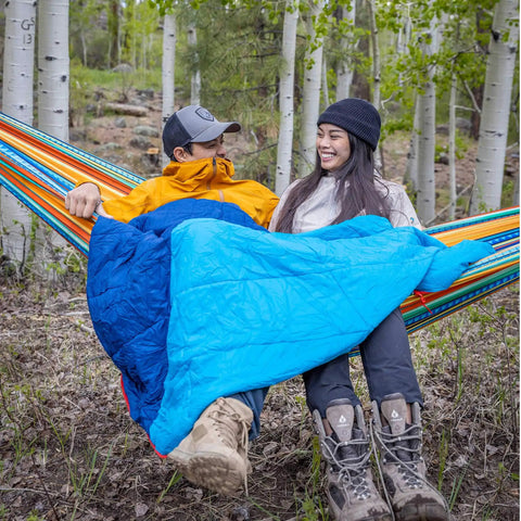 Couple in hammocks using ThermaQuilt Hammock Underquilt 40F 3 In 1 Go-To System For Outdoor Sleep, hiking boots, forest setting.
