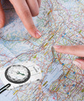 Hands pointing on a map with Three Pack Trail Ready Hiking Compass With Declination Scale For Backpacking And Camping, showing size and scale.