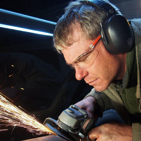 Person using angle grinder wearing ultra comfortable safety ear muffs with 31.5 dB SNR noise reduction, goggles, and jacket.