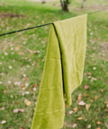 Green microfiber towel hanging on a line outdoors, suitable for travel and camping. Quick dry and lightweight. Size: 30 x 50 inches.