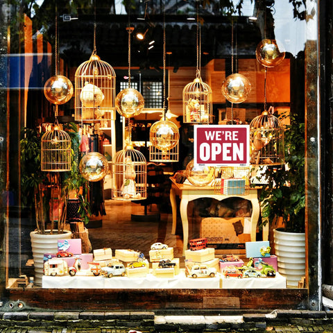 Storefront window with "We're Open" sign and decorative birdcages inside, showcasing Open And Closed Sign 12x16 Inch Double Sided Vinyl Sign.