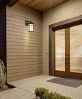 10.25 Inch Black And Clear Outdoor Wall Lantern with Integrated LED mounted on wooden siding near entryway.