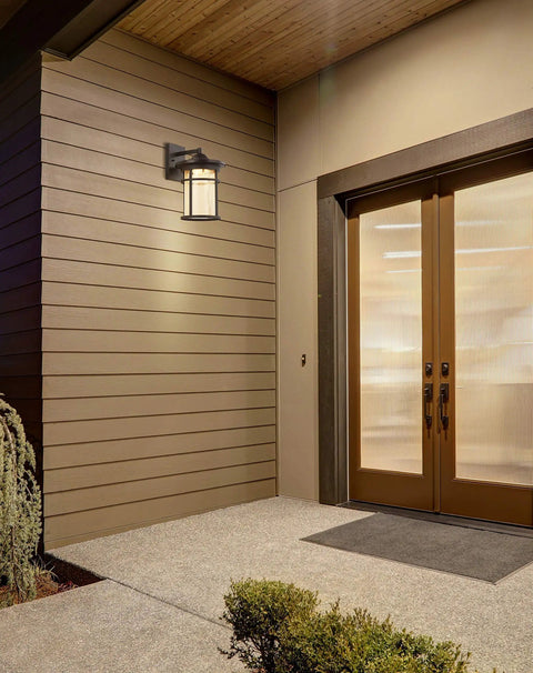 10.25 Inch Black And Clear Outdoor Wall Lantern with Integrated LED mounted on wooden siding near entryway.