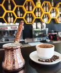 Top Notch Solid Copper Cezve for Turkish Greek Arabic Coffee with engraved finish and wooden handle next to coffee cup in cafe