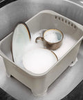 Gray heavy duty plastic sink wash basin for dishes with drain plug, filled with soapy water and tableware inside standard sink