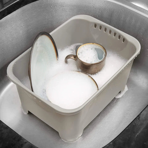 Gray heavy duty plastic sink wash basin for dishes with drain plug, filled with soapy water and tableware inside standard sink