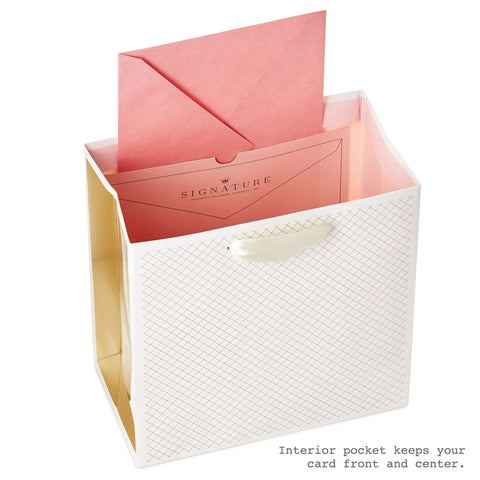 White gift bag with gold accents, pink envelope, and satin ribbon handles, featuring medium pink floral birthday gift bag with tissue paper.