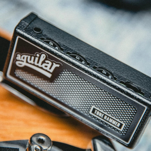 Close-up of Tone Hammer Inspired Bass Guitar Headphone Amp With Dual Analog Channels, textured black finish, on a blurred background.