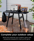Outdoor setup with Woodfire Outdoor Perforated Pizza Peel, Lightweight Aluminum, Perforated Design to Shake Off Flour and Prevent Dough Sticking, Compatible With OO100 Series Outdoor Ovens, Gray and Black on table with pizza oven and accessories.