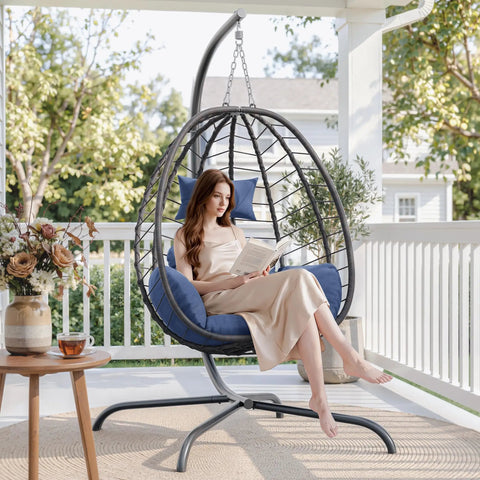 Woman reading on a Foldable Egg Chair With Stand For Indoor And Outdoor Use Wicker Rattan Swing Chair 485 Lbs Capacity Strong Iron Frame UV Resistant Cushion Patio Balcony Blue on a patio.