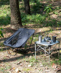 Ultralight Low Profile Camping Folding Chair With Side Pocket And Carry Bag 7.5 Inch Seat Height next to a foldable table outdoors.