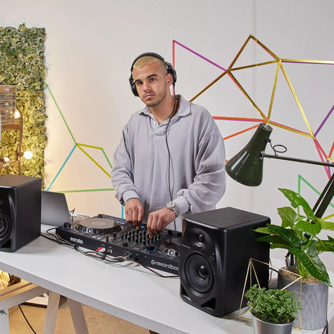 DJ using DM 50D BT 5 Inch Desktop Monitor System With Bluetooth in a modern studio setup with geometric wall art and greenery.