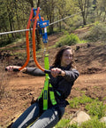 Person using Zip Line Trolley With Brake Featuring The Real Deal Patent No Wear Braking System, attached to line with green harness.