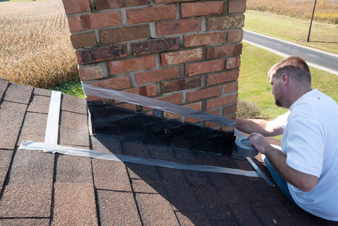 Man applying chimney flashing sealer and roof sealant that keeps water out, flexible waterproof sealant for chimney and roof flashing.