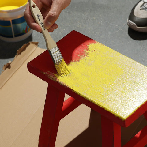 Applying yellow paint with 1 Inch Natural Bristle Paint Brush Set 16 Pack For Chip Painting on a red wooden stool outdoors