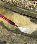 Red Beefy High Power Pressure Washer Gun With 40 Inch Wand Extension in use on a dirty pavement, showing water spray.