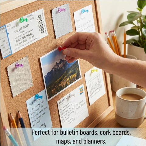 Hand placing red push pin on bulletin board surrounded by assorted notes and photos. Bulk Assorted Push Pins For Bulletin Boards Featuring Hella Bright Plastic Heads And Sharp Metal Tips That Gonna Keep Your Notes Secure And Organize Your Space Like A Pro.