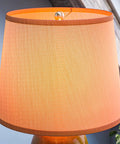 Close-up of Elaine Table Lamp With Antique Mercury Glass And Brushed Steel Finish, featuring white drum shade under warm lighting.