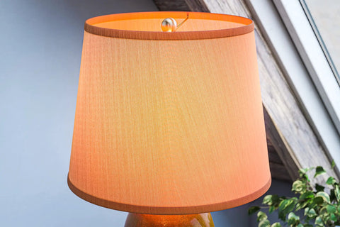 Close-up of Elaine Table Lamp With Antique Mercury Glass And Brushed Steel Finish, featuring white drum shade under warm lighting.