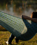 Person relaxing in Brazilian Style Mesh Hammock In A Bag 55 Inch Wide Light Blue Palm Tree Travel Hammock, outdoor setting