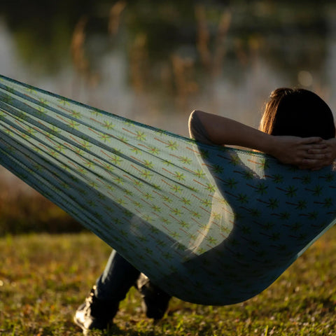 Person relaxing in Brazilian Style Mesh Hammock In A Bag 55 Inch Wide Light Blue Palm Tree Travel Hammock, outdoor setting