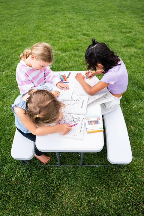 Three children coloring on a Compact Kids Picnic Table With Foldable Benches Under The Table And Built In Carry Handle For Easy Transport.