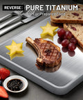 Two In One Titanium And Ebony Wood Cutting Board With Handle And Juice Groove showing steak and fruits on titanium surface