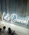 Lit Dance Neon Sign With Dimmer For Wall Decor Large LED Neon Light, "Let's Dance" text against rustic wood panel backdrop.