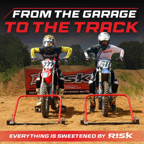 Two motocross riders on dirt bikes poised at the starting line with a banner in the background, ready for the race.