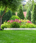 Six Piece White Garden Fence Set With Six Fence Inserts, Plastic Picket Edging for flower beds in a lush backyard.
