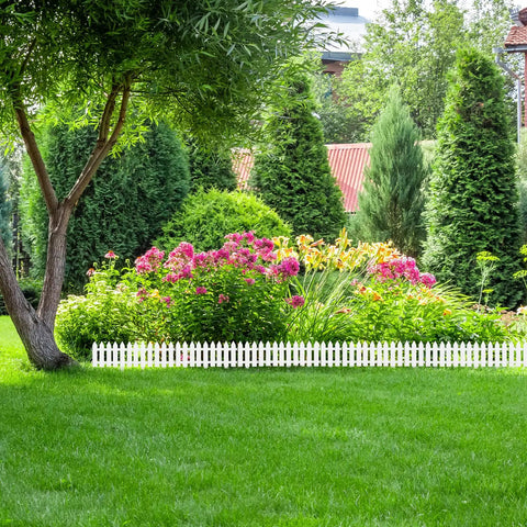 Six Piece White Garden Fence Set With Six Fence Inserts, Plastic Picket Edging for flower beds in a lush backyard.