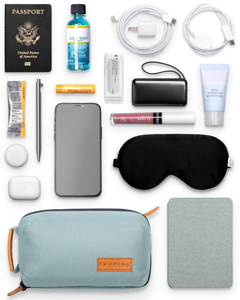 Compact Travel Tech Organizer Bag with leather accents, dusty teal, surrounded by travel essentials for cables and gadgets