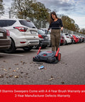 Heavy Duty Turbo Hand Sweeper With Dual Disc Brushes And Beltless Drive Works Like A Super Champ Crushing Fine Dust And Grime Across A 75 Centimeters Sweep Path in use in a parking lot.