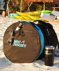Next Descent bag with tumbler and sunglasses on sandy beach near kayaks