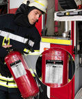 Firefighter using fire extinguisher with inspection tag near fire truck, close-up of inspection record visible.