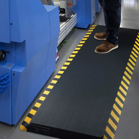 Anti Fatigue Industrial Standing Mat With High Density Memory Foam Ergonomic Floor Pad For Work Tables Reducing Leg And Back Strain 20x59 Inches Yellow Border 1 Piece shown installed in industrial setting