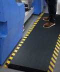 Anti Fatigue Standing Mat For Workstation Ultra Cushy High Density Memory Foam Ergonomic Floor Pad To Fight Leg And Back Pain Industrial Grade Durability 24 By 70 Inches With Yellow Border placed in front of machinery